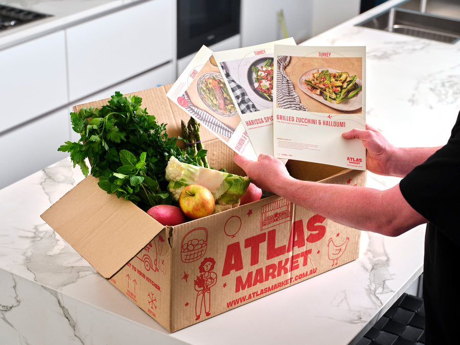 Recipe cards lifted out of a Cuisine Box full of fresh produce