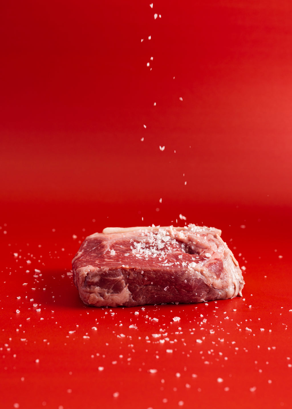 Raw meat being sprinkled with salt on a red background