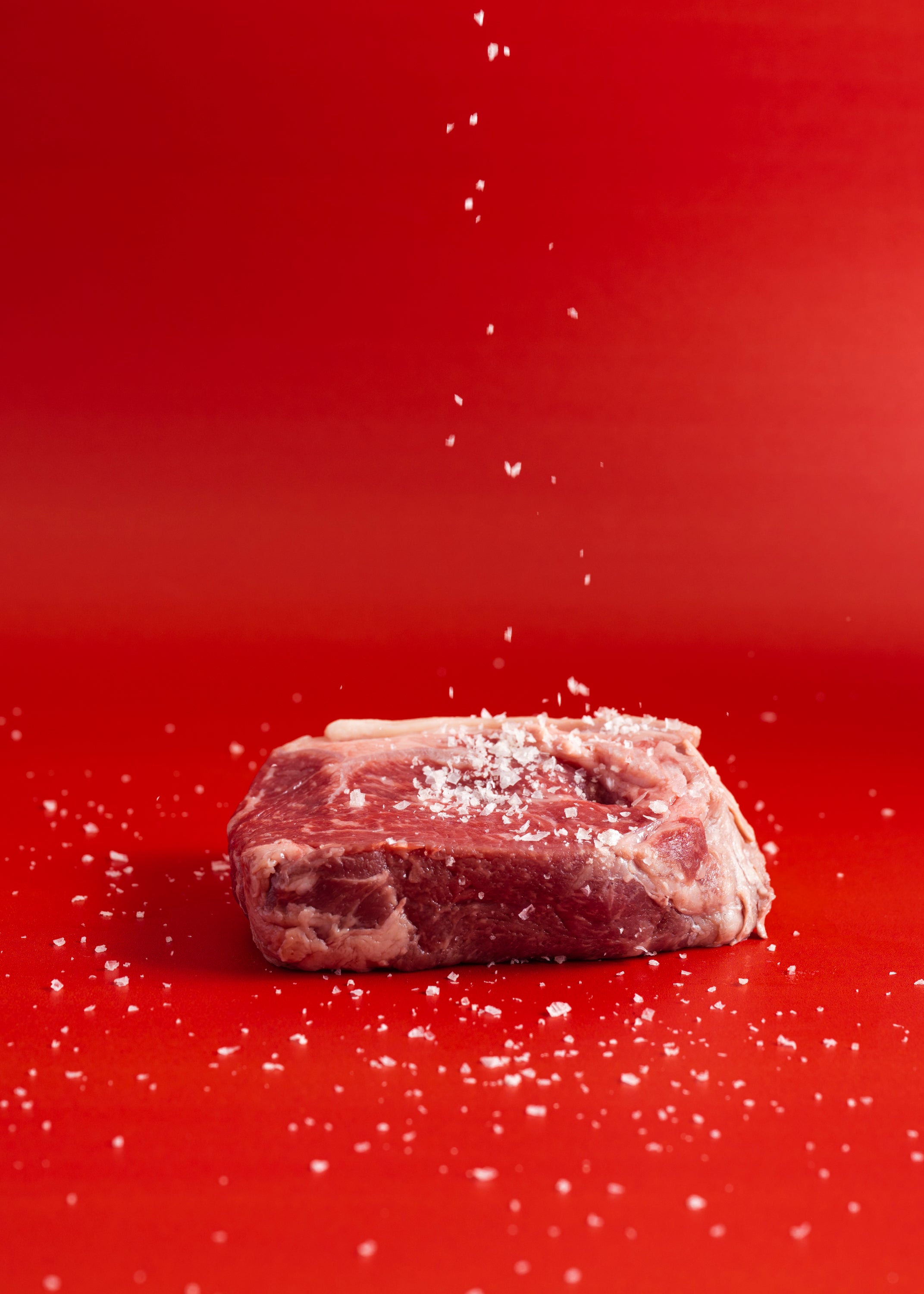 Raw meat being sprinkled with salt on a red background