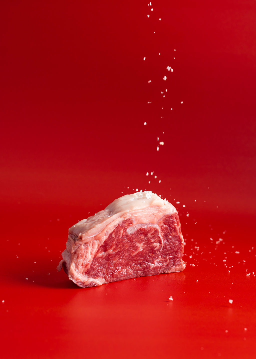 Raw beef cube with salt being sprinkled on a red background